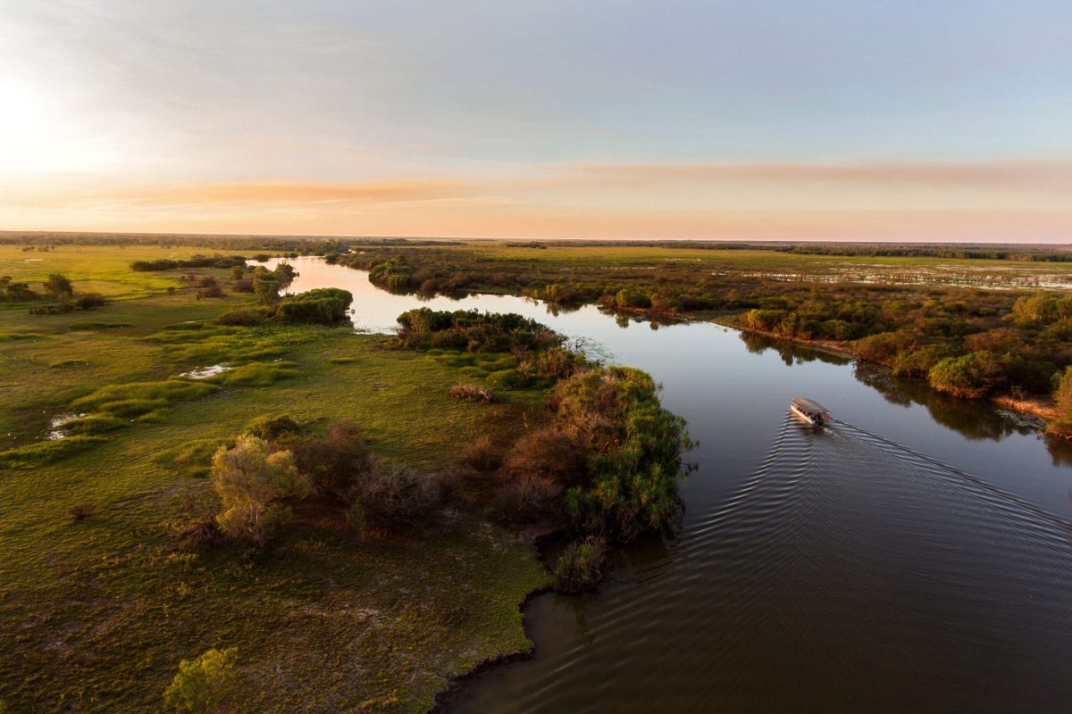A boat travels along a winding river through lush green landscape at sunset.