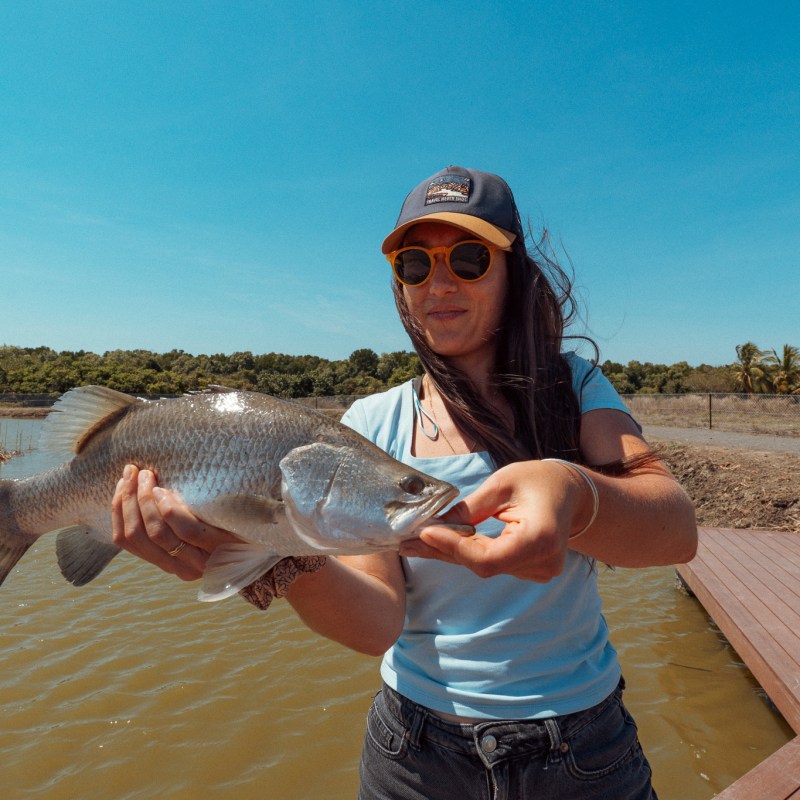 Woman holding a large fish by a lake on a sunny day.