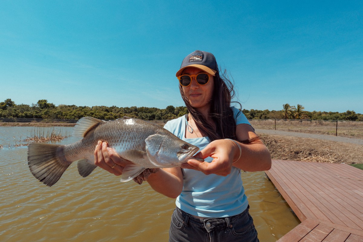 Woman holding a large fish by a lake on a sunny day.